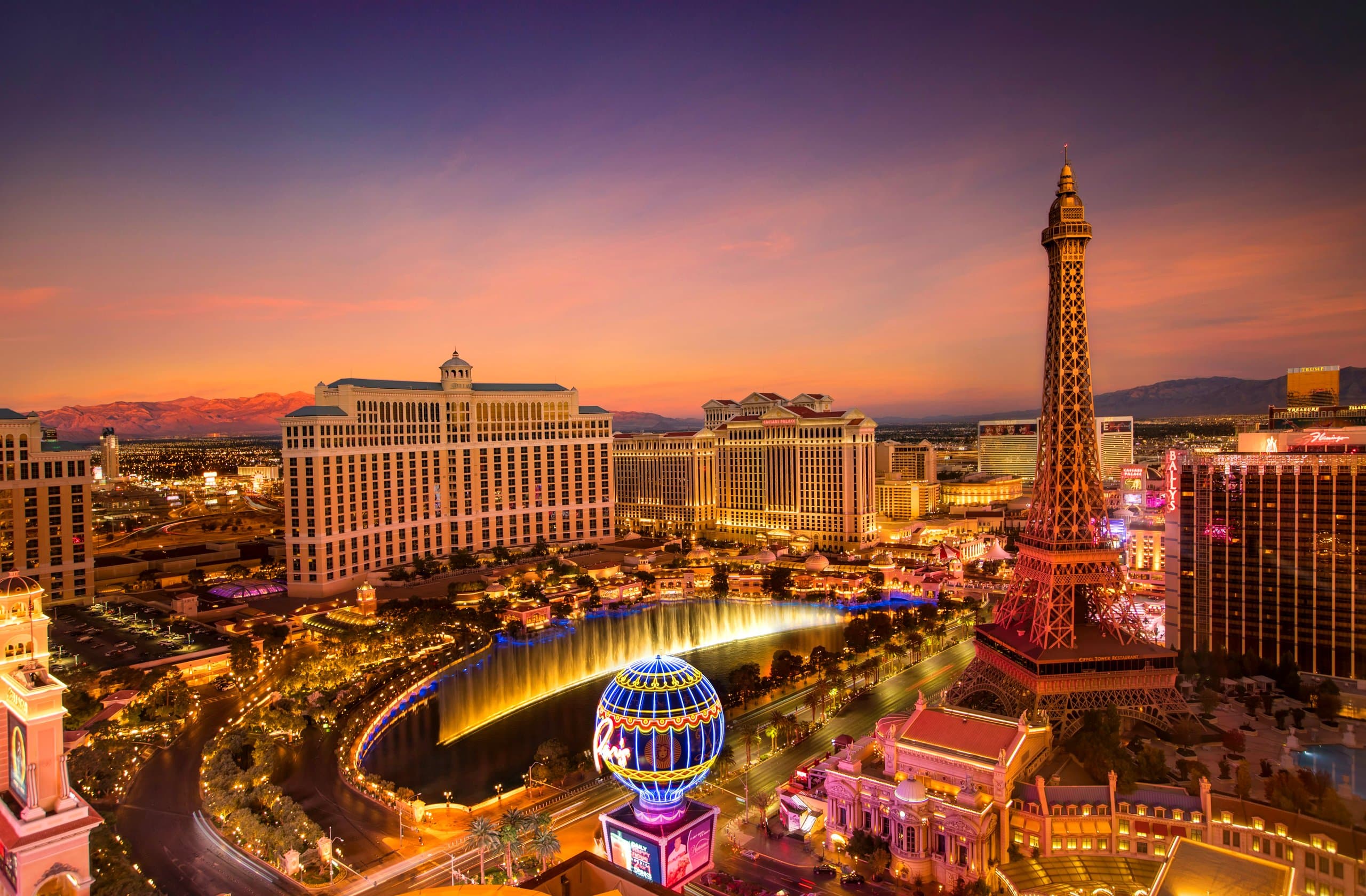 The Las Vegas Strip at dusk, with the Bellagio fountains and the Eiffel Tower replica lit up against a sunset sky